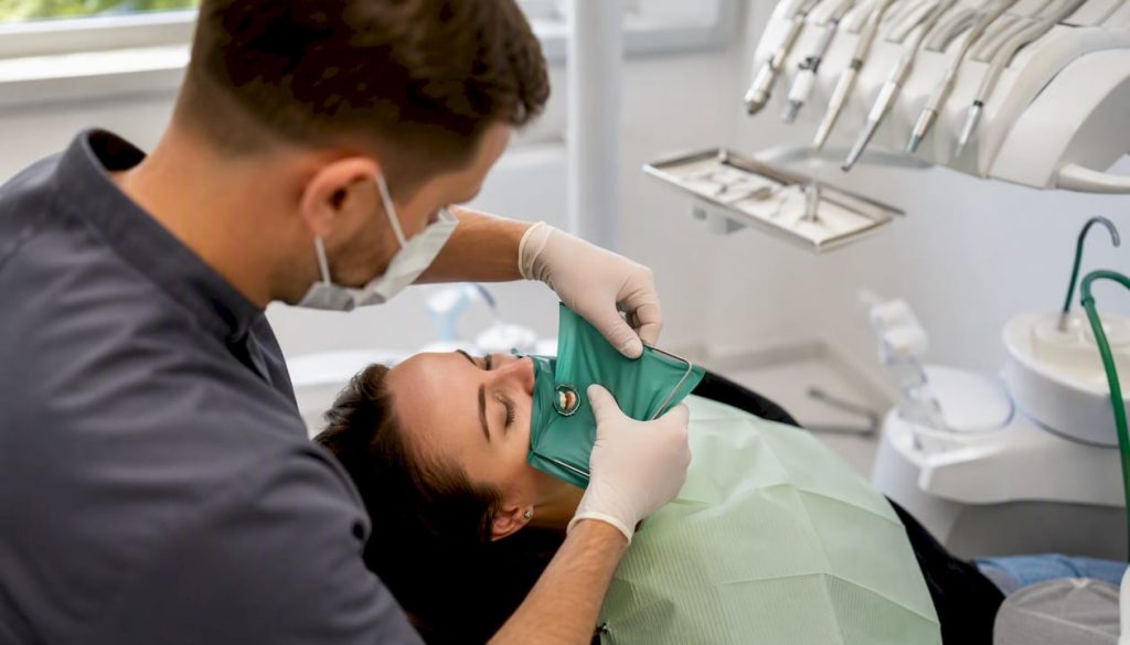 Medicul stomatolog izolează un dinte cu ajutorul unui digă de cauciuc pentru a-l trata în condiții optime.