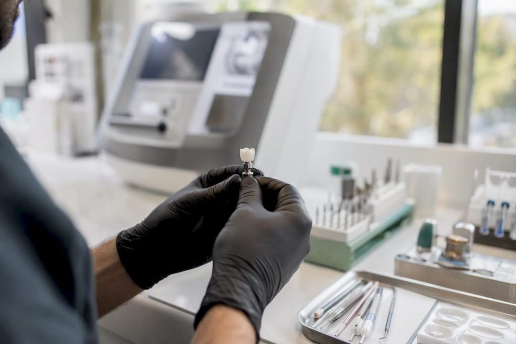 Mâini care țin o coroană dentară prelucrată prin frezare