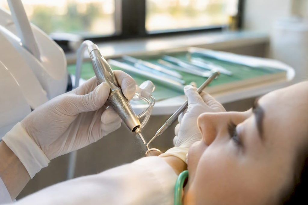 Mâini care efectuează detartraj subgingival cu instrumente dentare